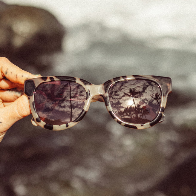 Sunglasses with a reflective surface held by a hand against a blurred natural background