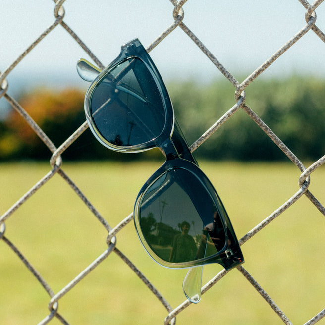 Black sunglasses with reflective lenses on a chain-link fence with a blurred outdoor background