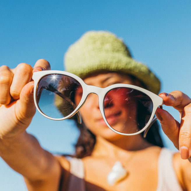 Person holding white sunglasses with a clear blue sky background