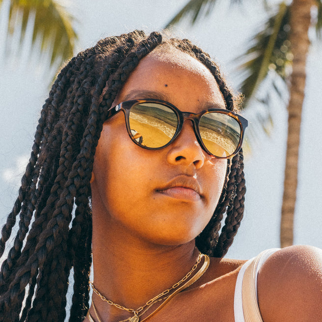 Person wearing sunglasses with palm trees in the background