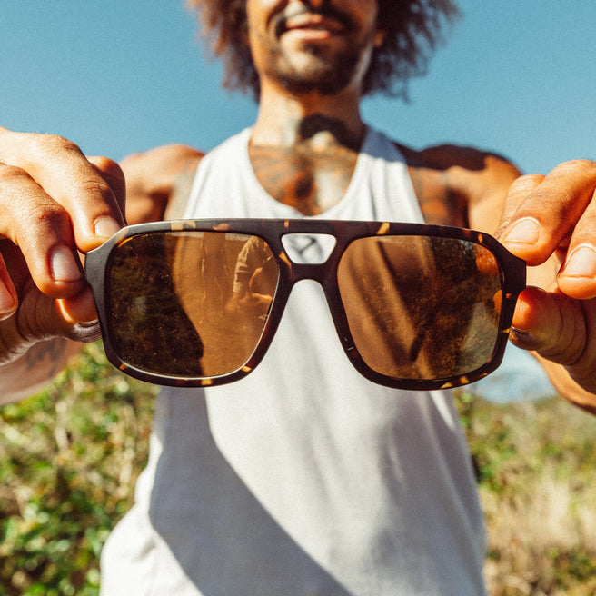 Person holding sunglasses with a blurred natural background