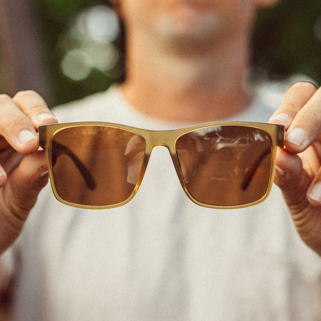 Person holding a pair of brown sunglasses with a blurred background