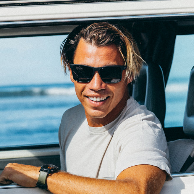 Man wearing sunglasses and a white shirt sitting inside a vehicle with a scenic background