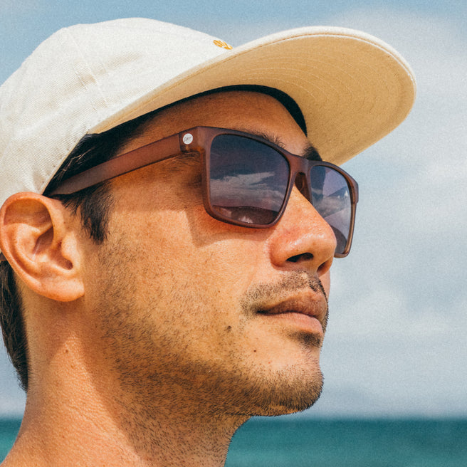 Man wearing sunglasses and a cap with ocean and sky in the background
