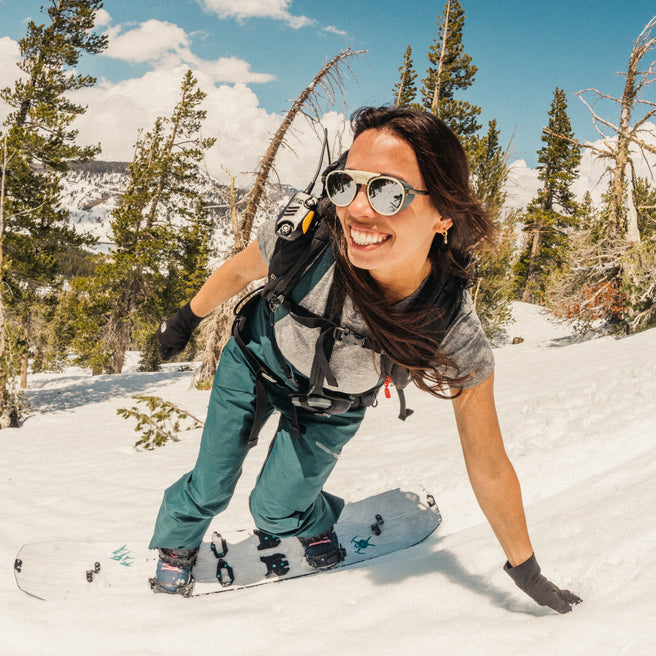 Person snowboarding in a snowy landscape with trees and a clear sky.