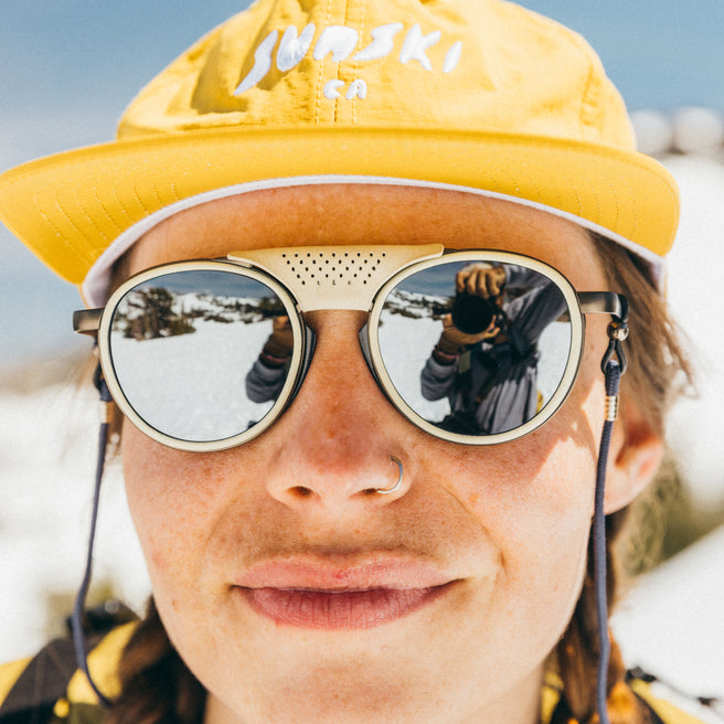 Person wearing a yellow cap and reflective sunglasses with a snowy landscape in the background