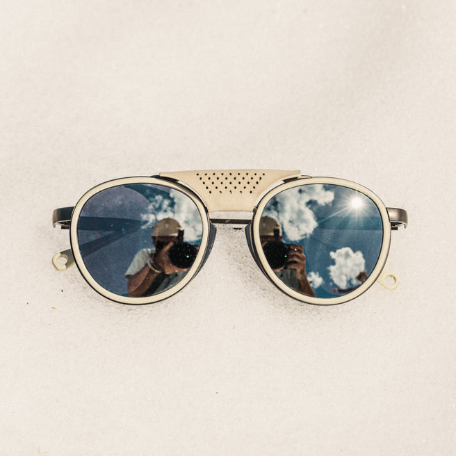 Sunglasses with reflective lenses showing a blue sky and clouds on a beige background