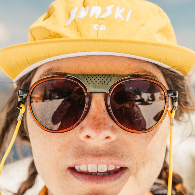 Person wearing a yellow 'Sunski' cap and round sunglasses with a blurred background
