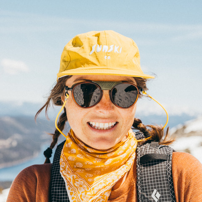 Person wearing a yellow cap and sunglasses with a mountainous background