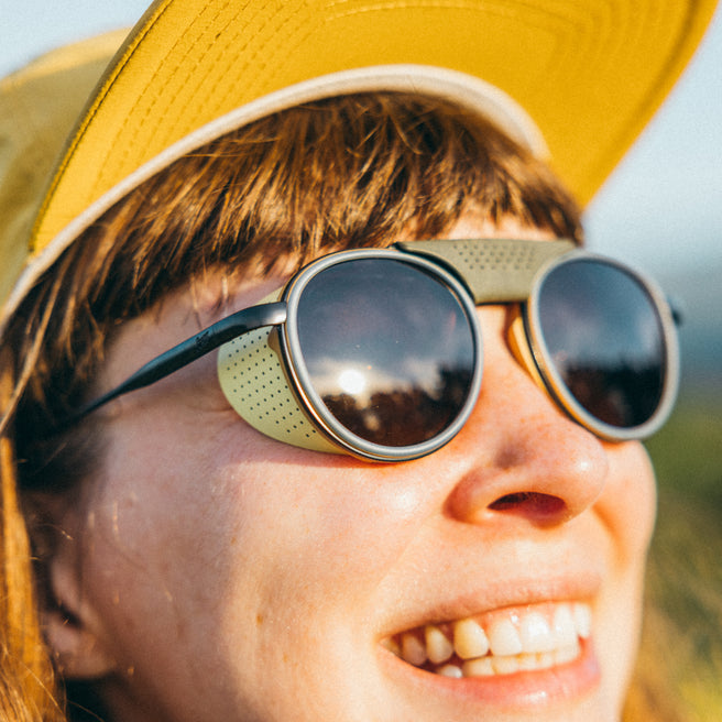 Person wearing a yellow cap and round sunglasses with a blurred natural background