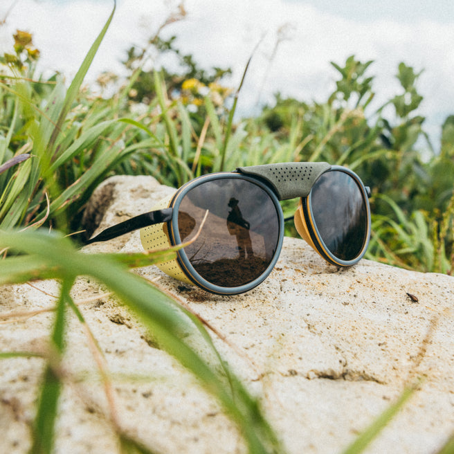 Sunglasses with green strap on a rock surrounded by grass and plants