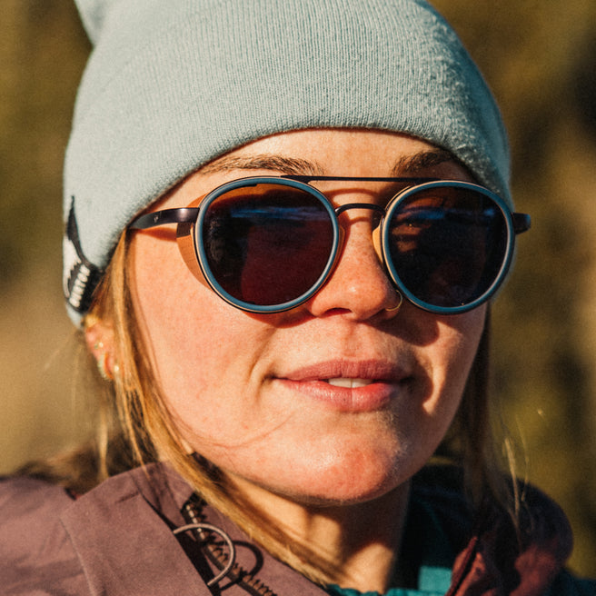 Person wearing sunglasses and a beanie with a blurred natural background
