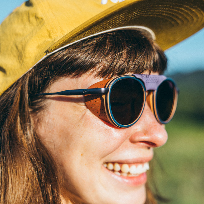 Person wearing a yellow cap and round sunglasses with a blurred natural background