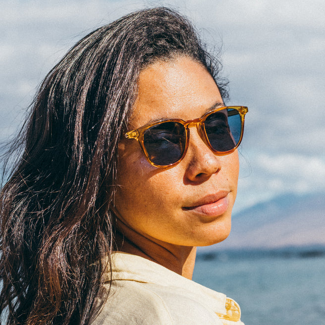 Woman wearing sunglasses with a scenic background of water and sky.