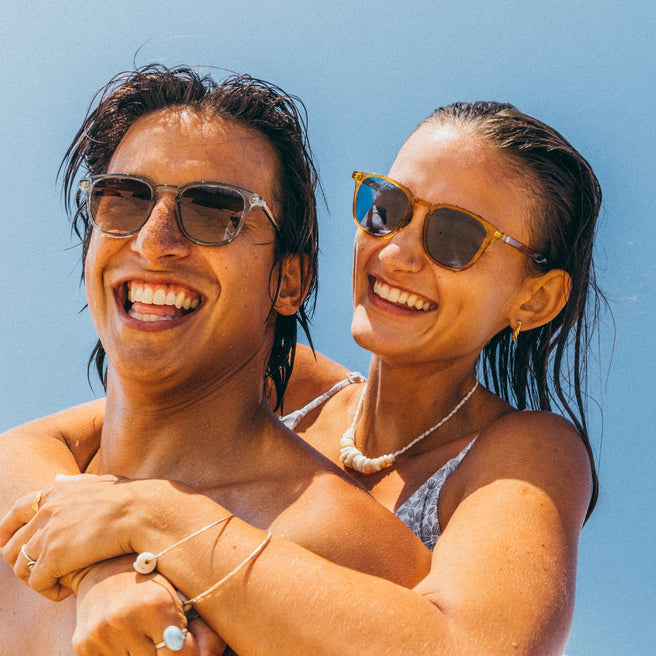 Two people with sunglasses smiling against a clear blue sky