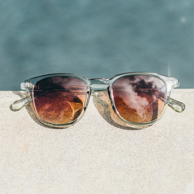Sunglasses with reflective lenses on a sandy surface with water in the background