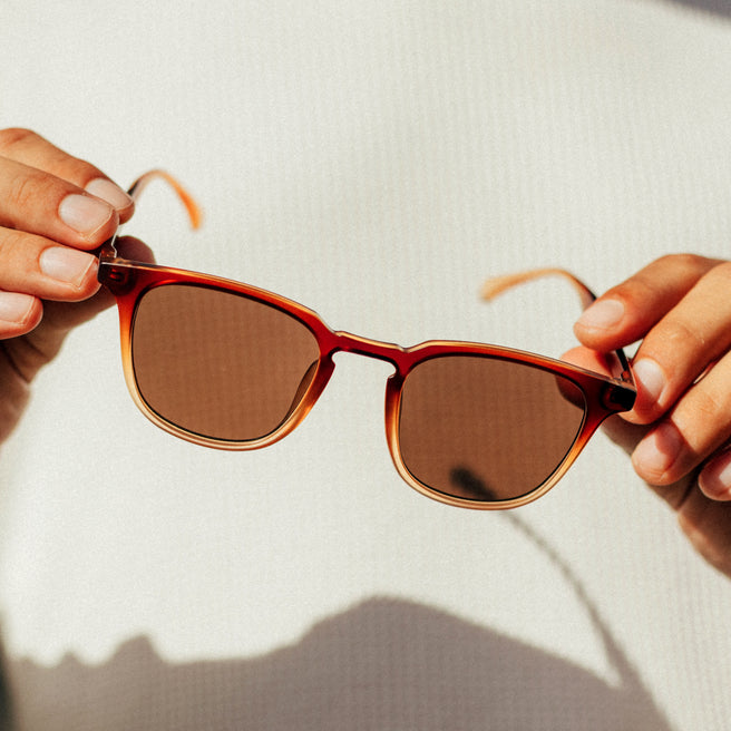 Sunglasses held by hands with a neutral background