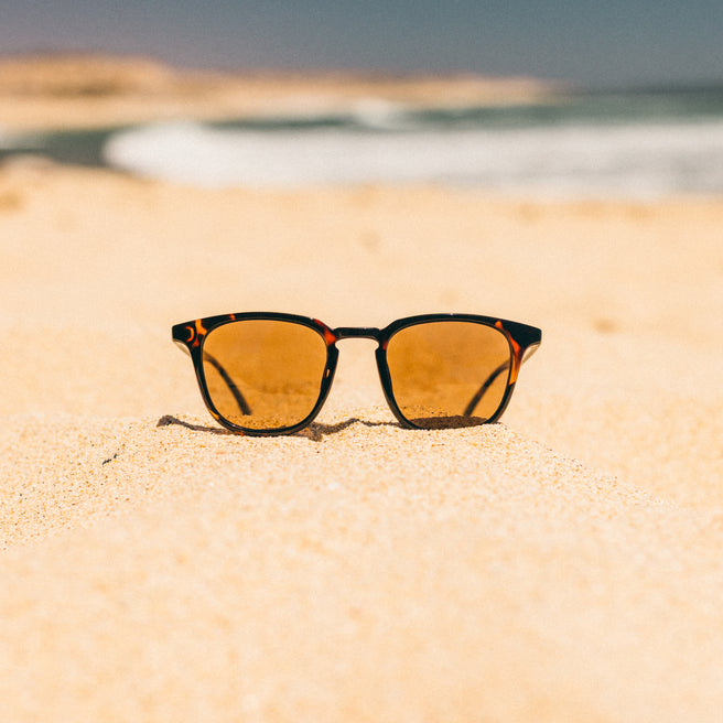 Sunglasses on a sandy beach with ocean in the background