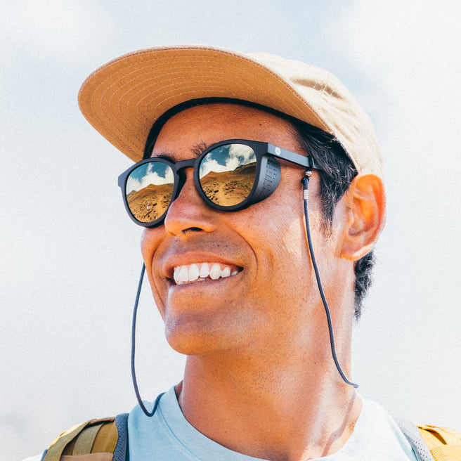Person wearing a cap and sunglasses with a reflective landscape.