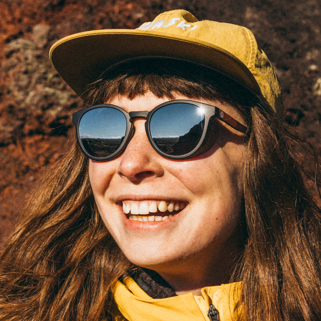 Person wearing sunglasses and a yellow cap with a mountainous background