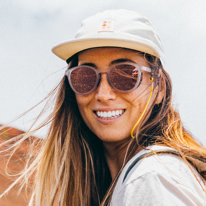 Woman wearing sunglasses and a cap with a neutral background