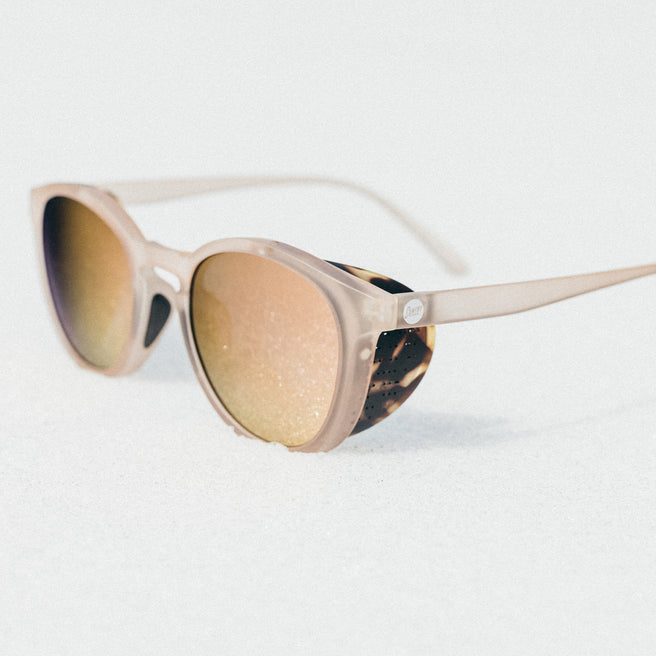 Sunglasses with a beige frame and reflective lenses on a white background