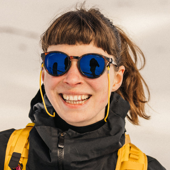 Person wearing sunglasses with blue lenses and a yellow backpack against a neutral background