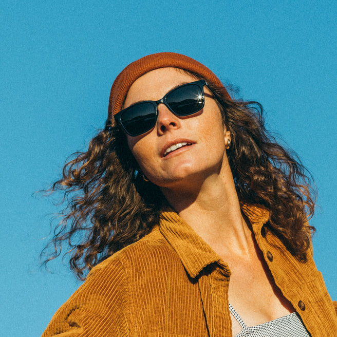 Woman wearing sunglasses and a brown beanie against a clear blue sky
