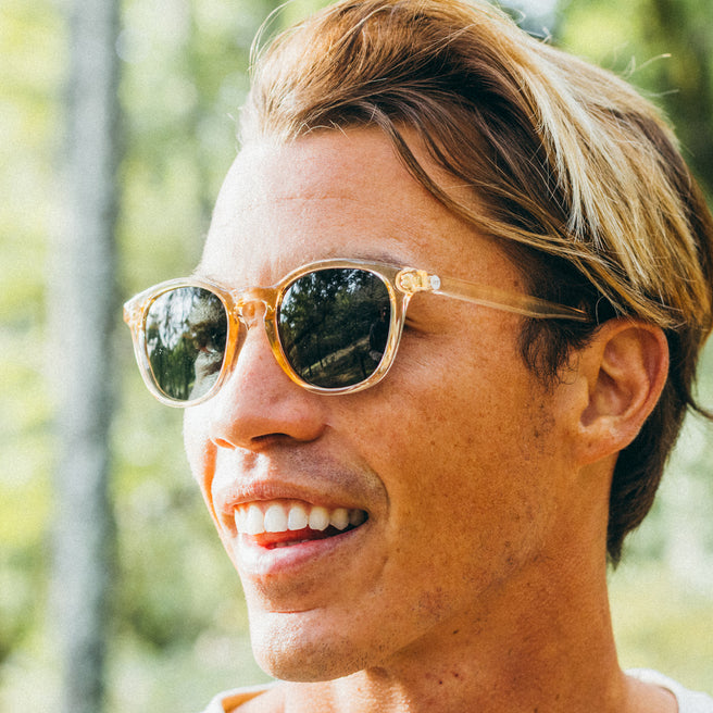 Person wearing gold-framed sunglasses with a blurred natural background