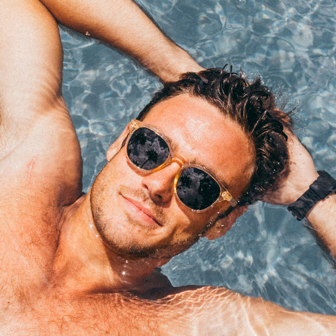 Man wearing sunglasses and a watch, lying in clear blue water.