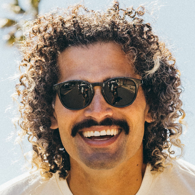 Man with curly hair wearing sunglasses against a light background