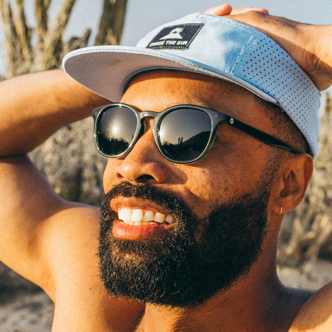 Man wearing sunglasses and a cap with desert landscape in the background