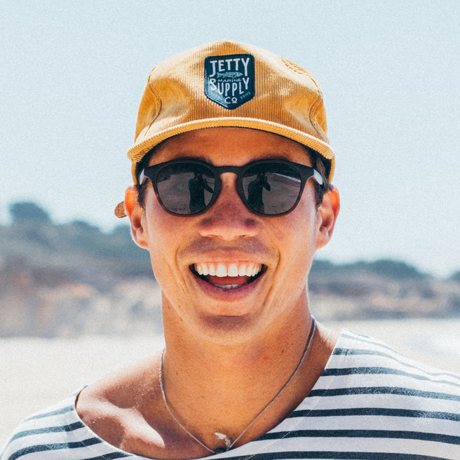 Man wearing a yellow cap with a brand logo and sunglasses, standing outdoors.