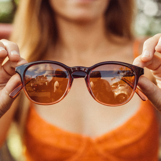 Person holding a pair of sunglasses with a blurred background