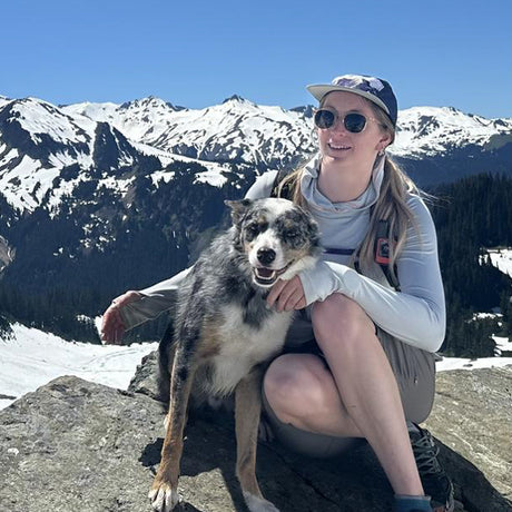 Woman and dog sitting on a rock with snow-capped mountains in the background