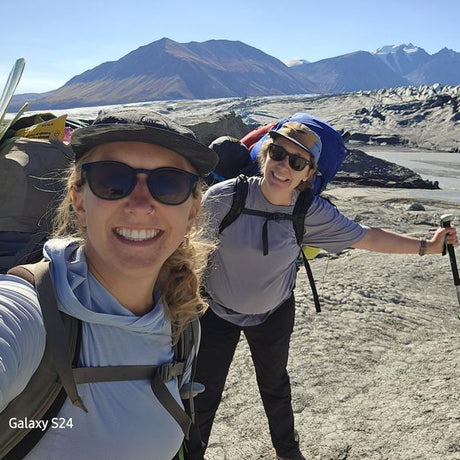 Two hikers taking a selfie on a mountain with backpacks and sunglasses.