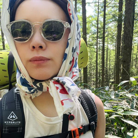 Person wearing sunglasses and a colorful headscarf with a forest background