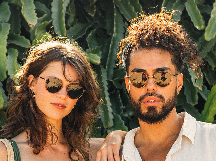 Two people wearing sunski sunglasses with a green leafy background
