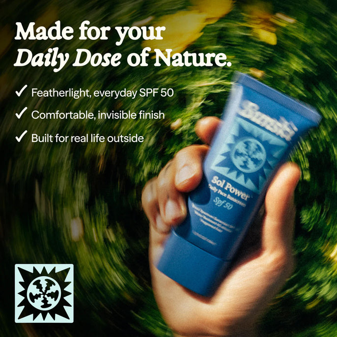 Hand holding a blue sunscreen tube with text about its features against a blurred natural background