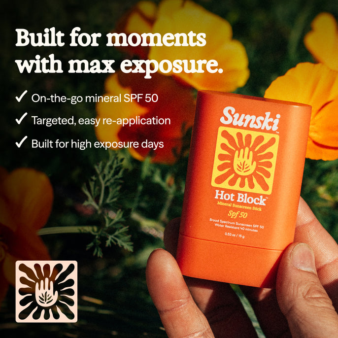 Sunski Hot Block sunscreen stick held by a hand with flowers in the background