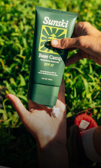 person applying base camp spf 45 sunscreen with grass in the background