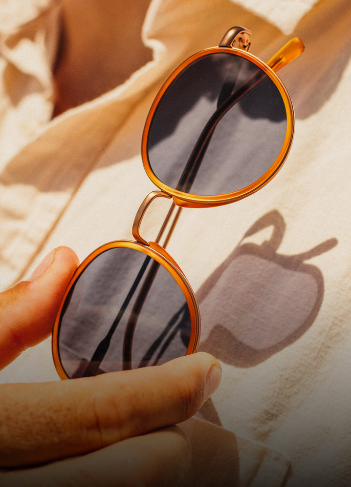 Round sunglasses with gold frame held by a hand on a textured surface