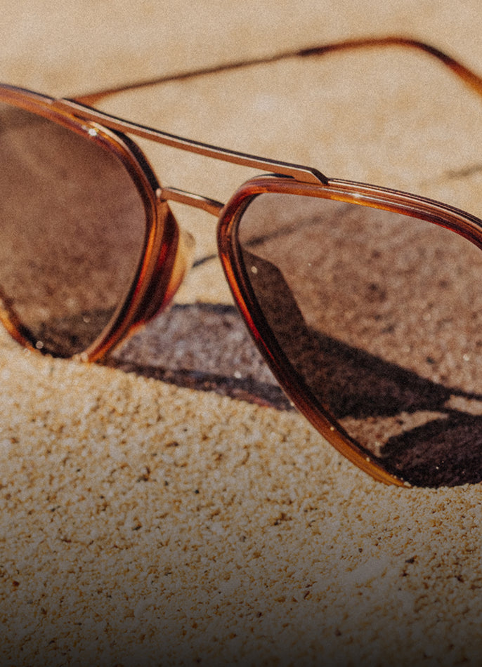 Sunglasses with brown lenses and gold frame on sand