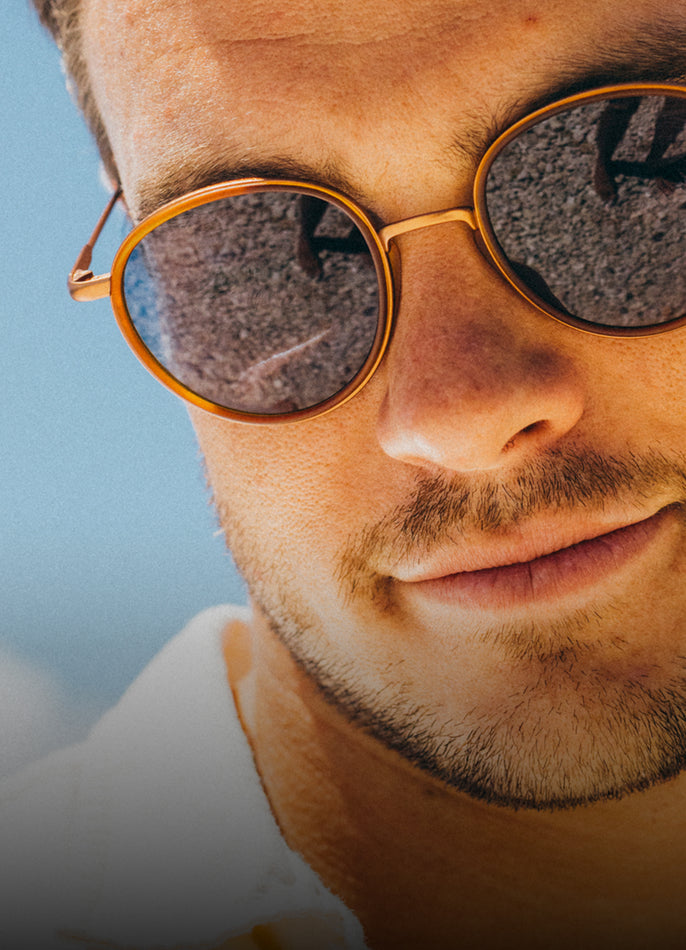 Close-up of a person wearing gold-framed sunglasses with a blurred background