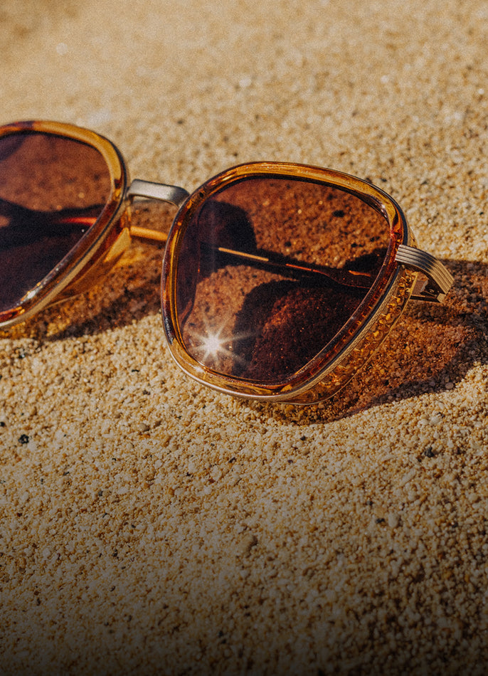 Sunglasses with brown tortoiseshell frame and lenses on a sandy surface