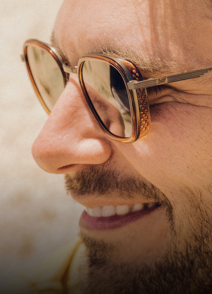 Close-up of a person wearing gold-rimmed sunglasses with a blurred background