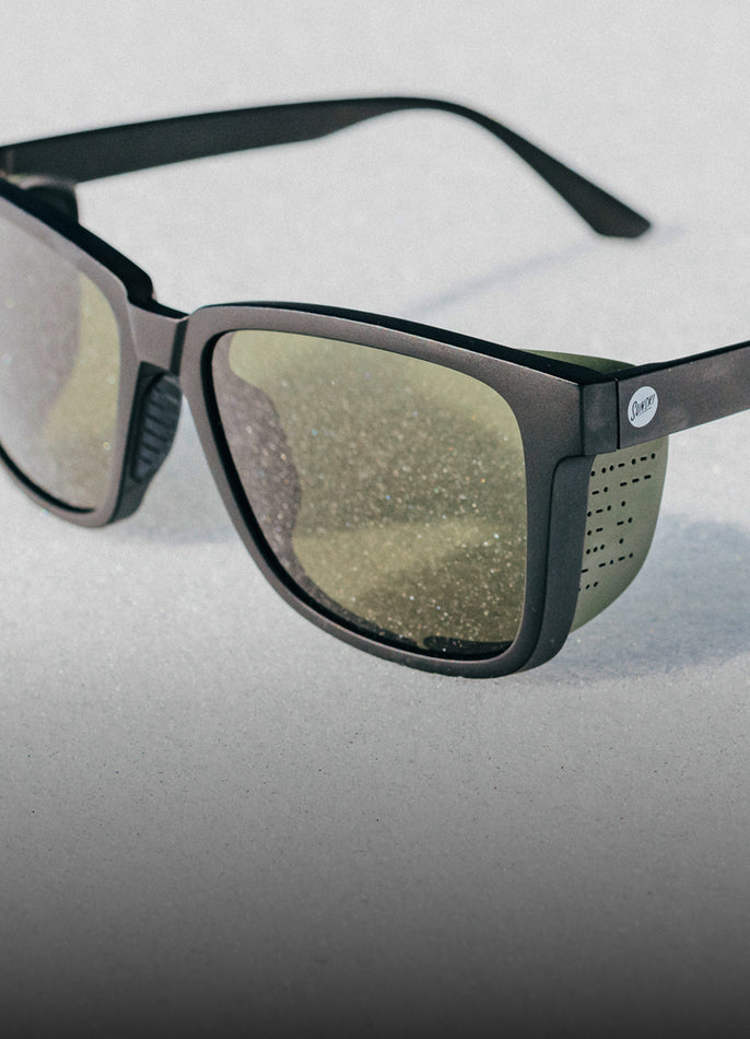 Sunglasses with black frame and reflective lenses on a light gray background