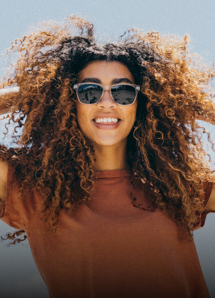 Woman with curly hair wearing sunglasses against a clear blue sky