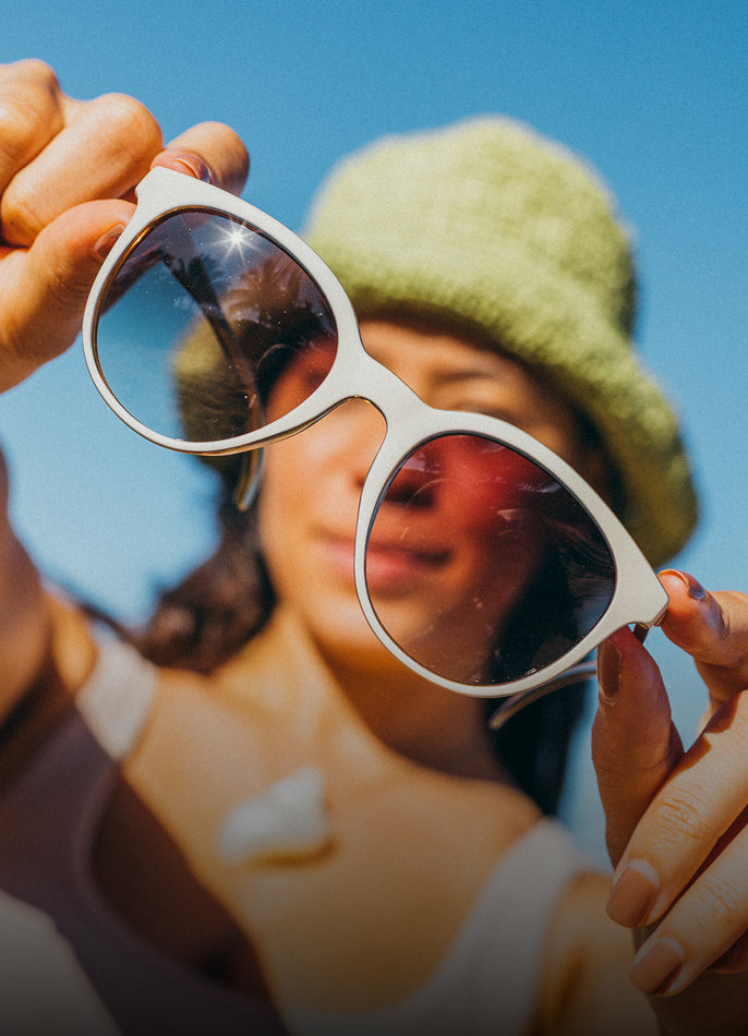 Person holding a pair of sunglasses with a clear blue sky background
