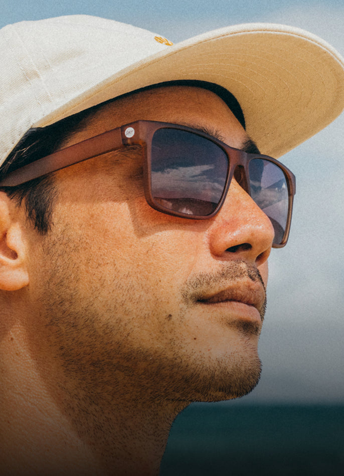 Man wearing sunglasses and a beige cap with a blurred natural background